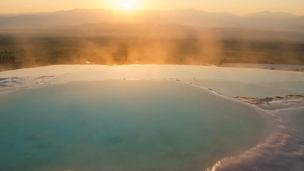 A drone flies over the Pamukkale travertines at sunset: white terraces and turquoise pools reflect the golden… Still from a video made with Seedance 2.5.
